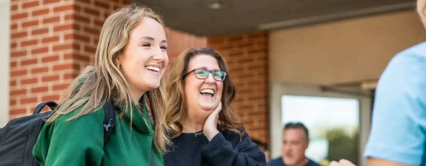 Student smiling with a parental figure outside